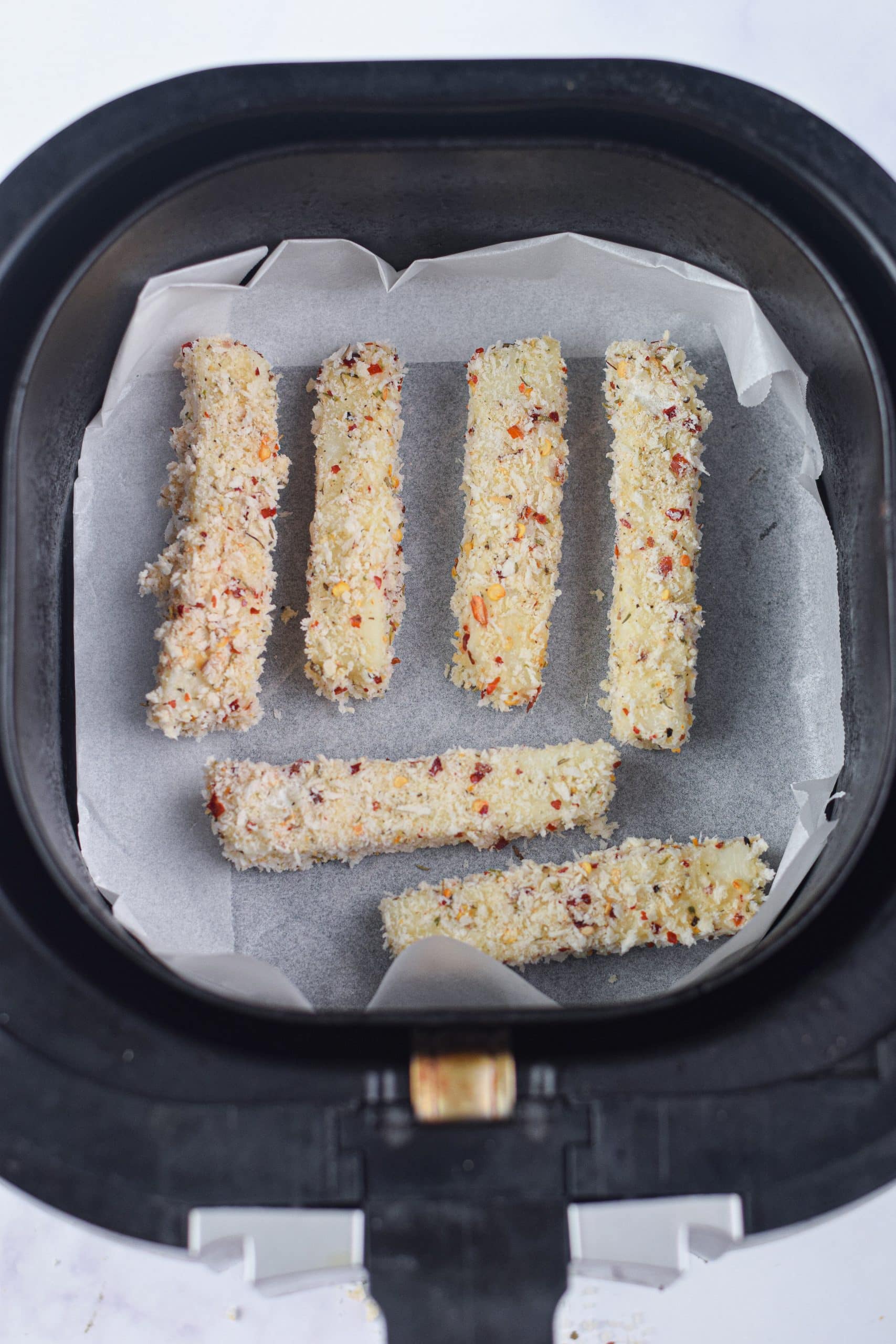 breaded mozzarella sticks in a parchment paper lined air fryer basket