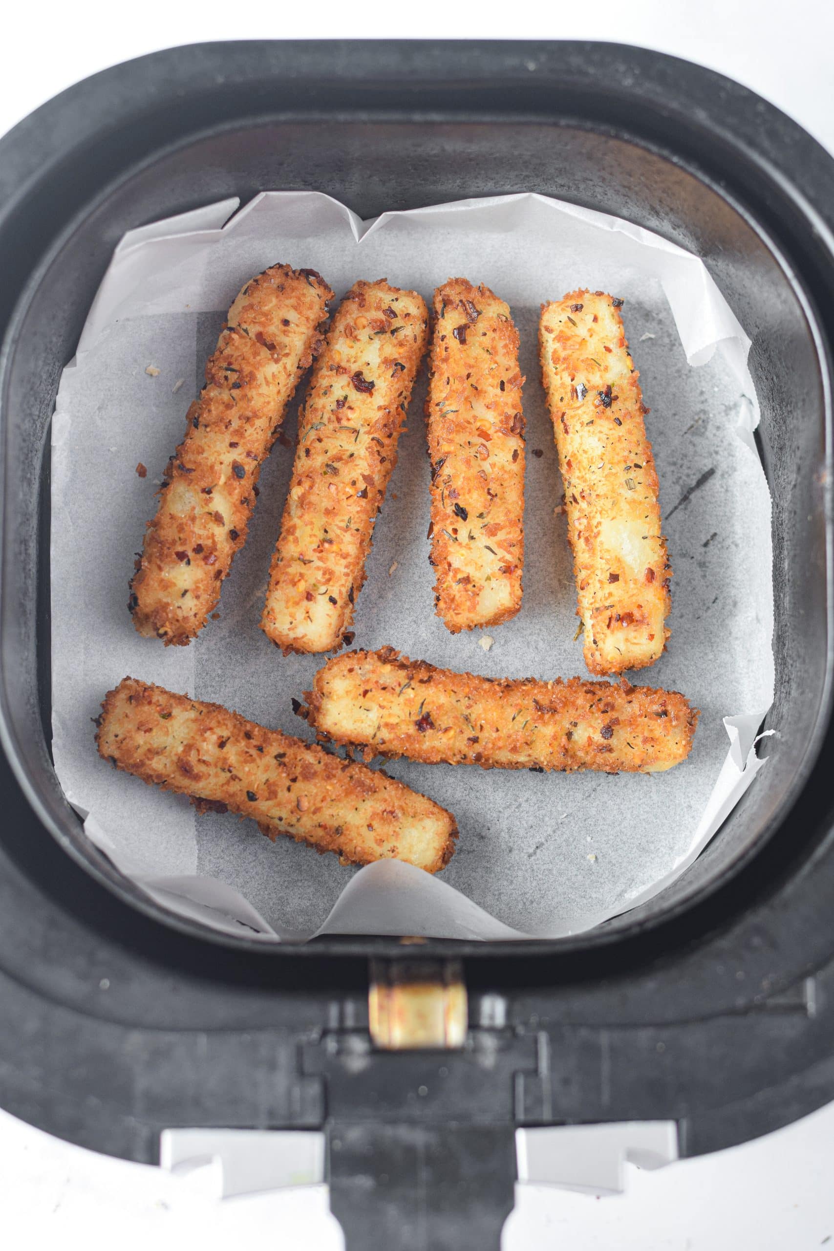 cooked mozzarella sticks in the parchment paper lined basket of an air fryer