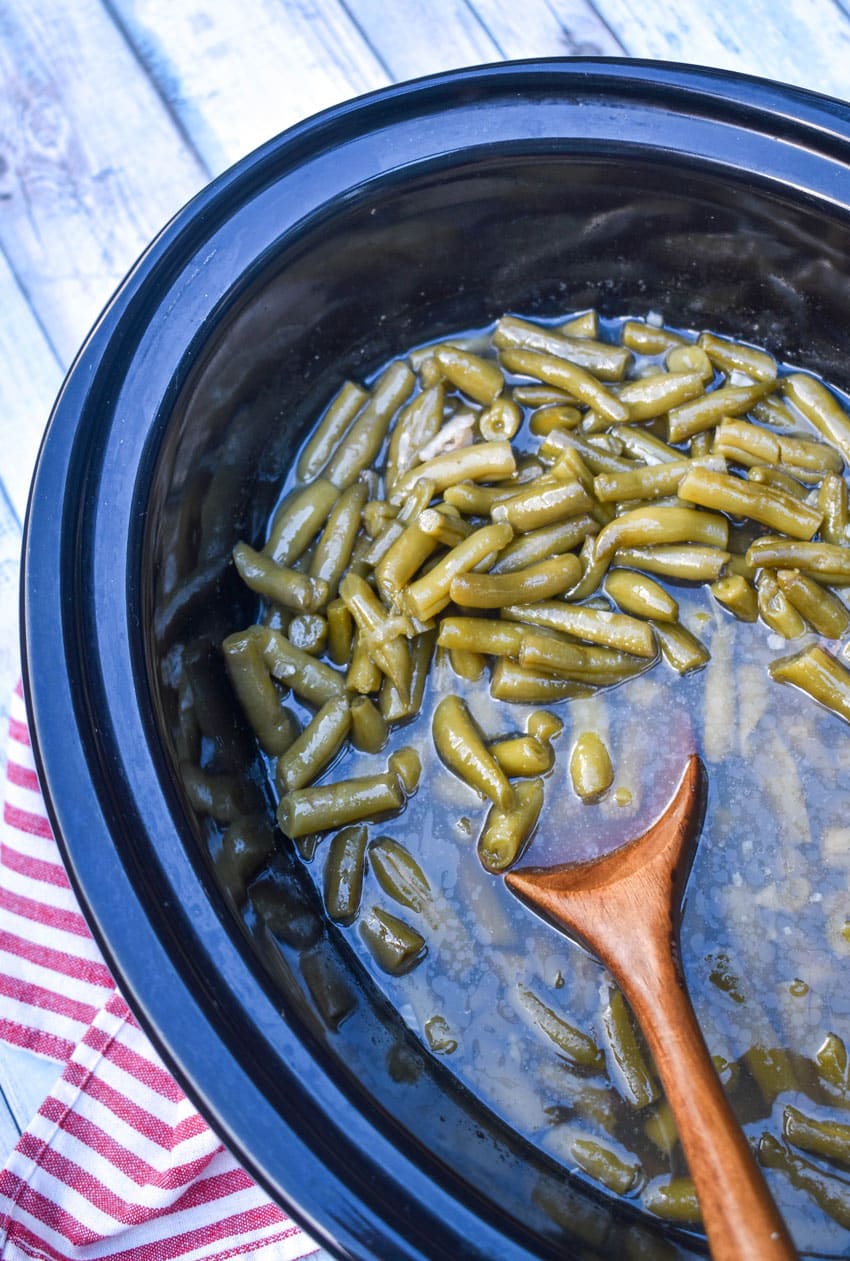 a wooden spoon in a crockpot filled with seasoned canned green beans