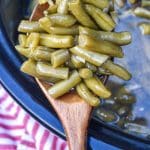 a wooden spoon holding up a scoop of slow cooker green beans