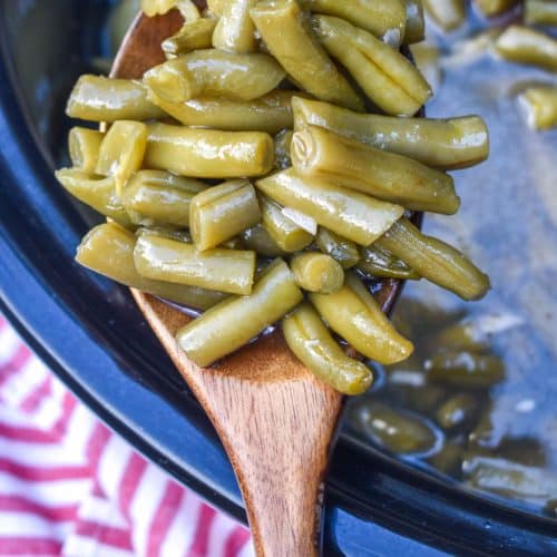 a wooden spoon holding up a scoop of slow cooker green beans