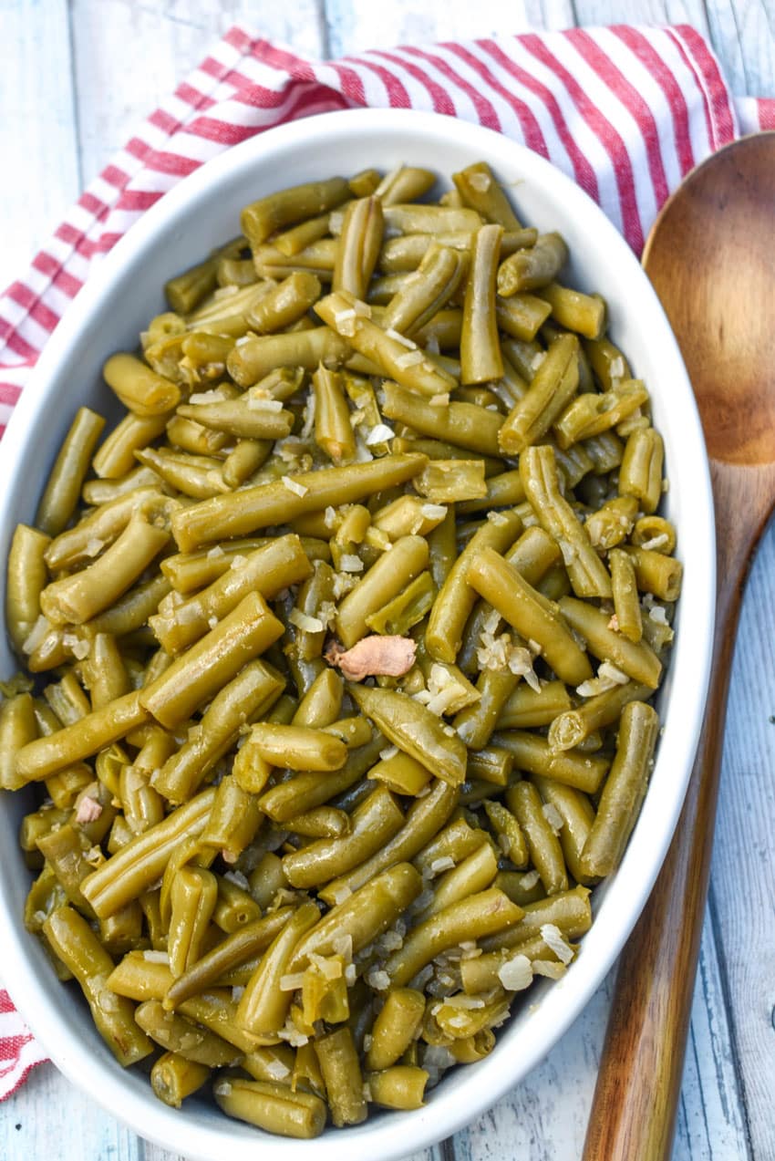 slow cooker green beans in a white serving bowl with a wooden spoon on the side