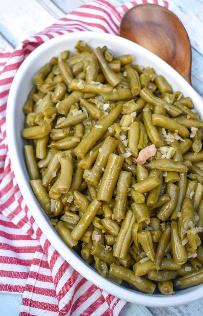 slow cooker green beans in a white serving bowl with a wooden spoon on the side
