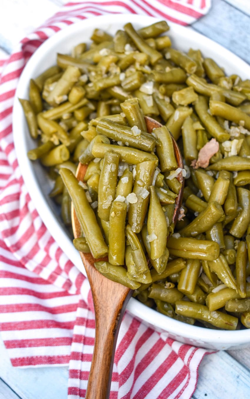 a wooden spoon holding a scoop of slow cooker green beans over a white bowl