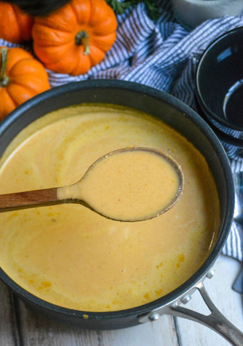 a wooden spoon holding up a scoop pf creamy pumpkin soup above a pot