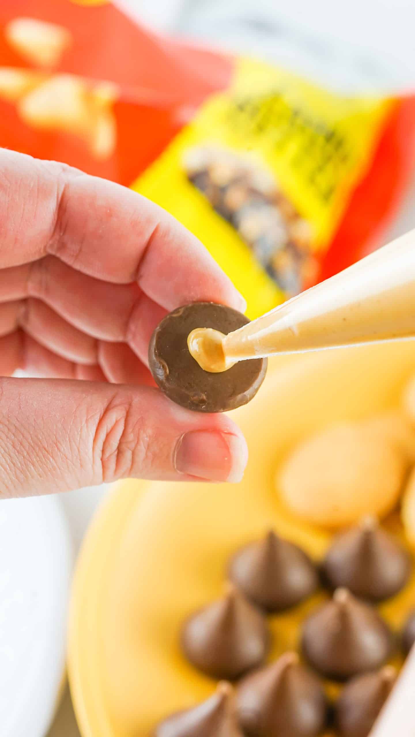 peanut butter being squeezed onto the bottom of an unwrapped hershey's kiss chocolate