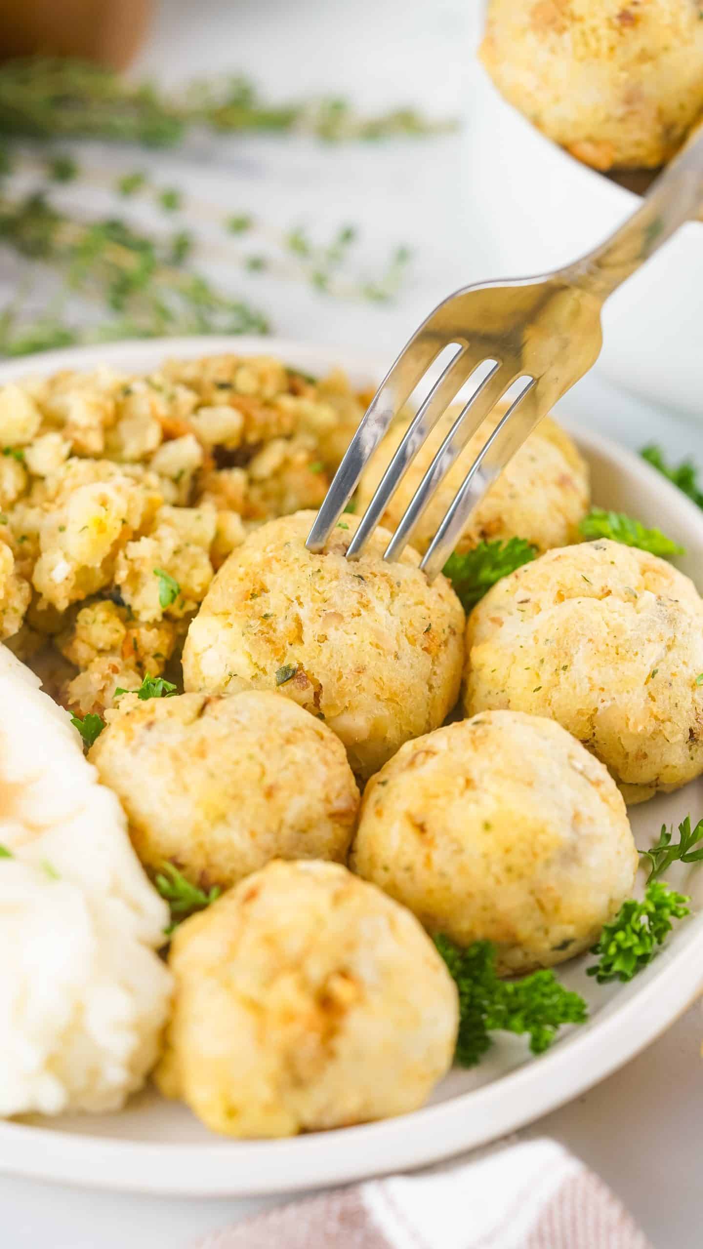 a silver fork stuck in a leftover turkey meatball on a white plate with fresh herbs
