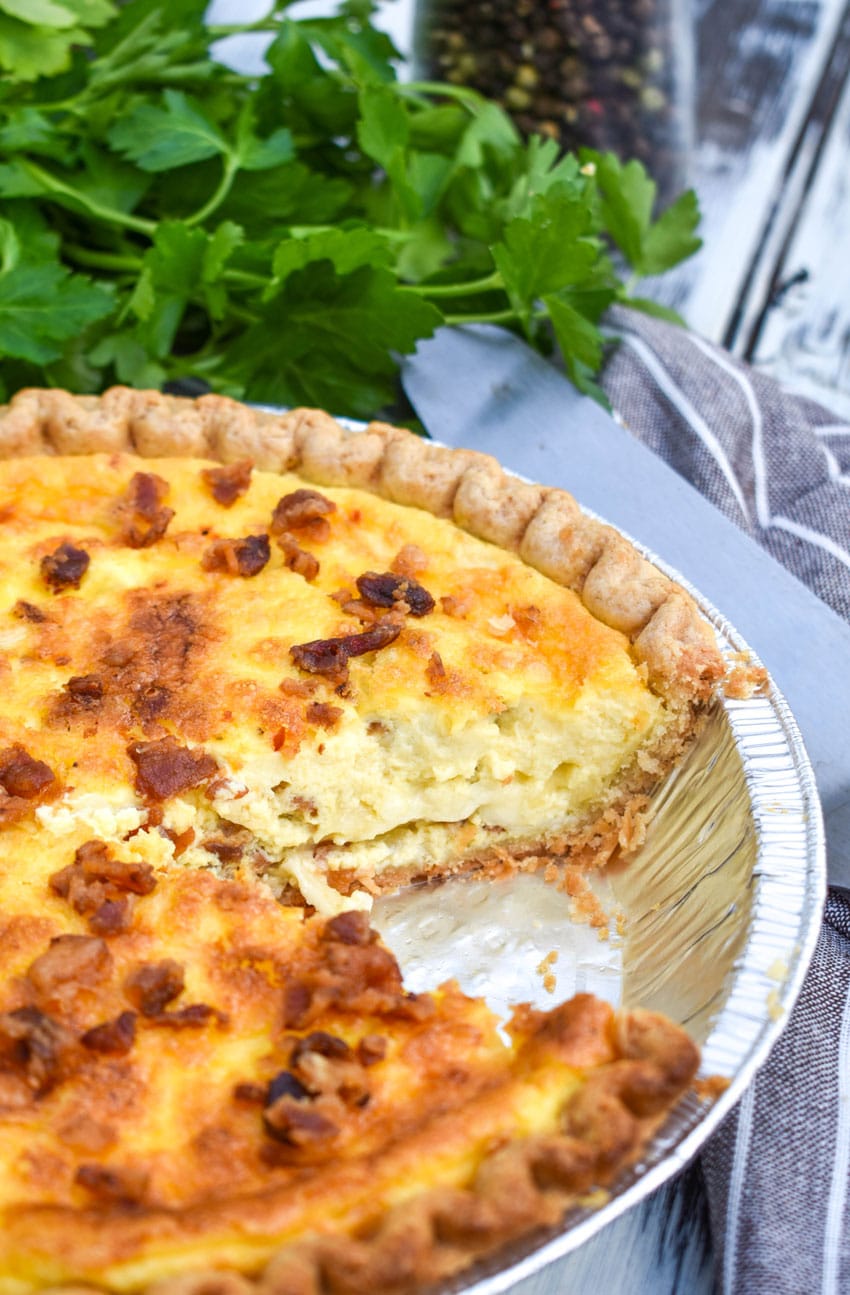 a bacon swiss quiche next to a bunch of fresh herbs