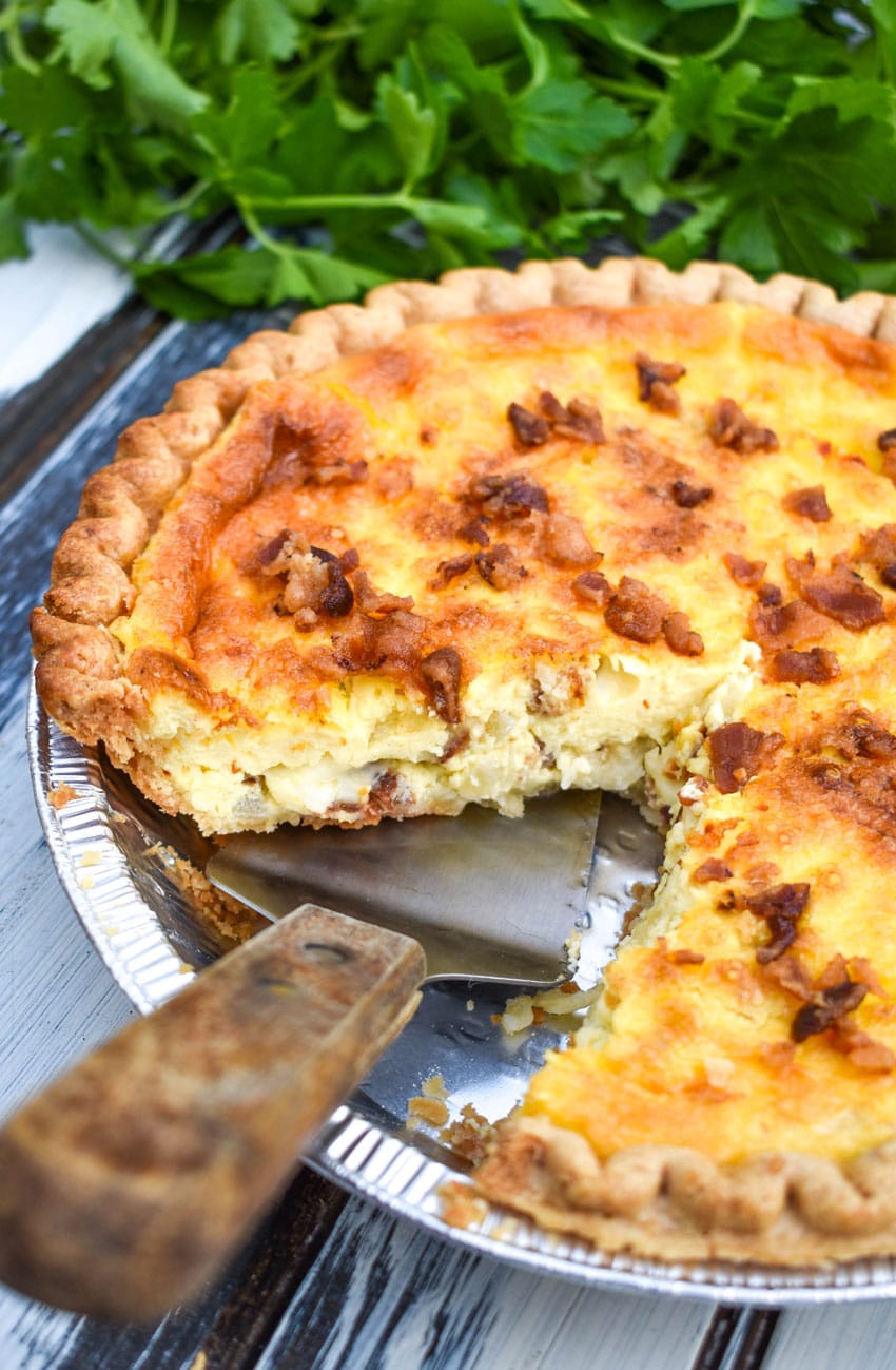 a wooden spatula lifting up a slice of bacon swiss quiche
