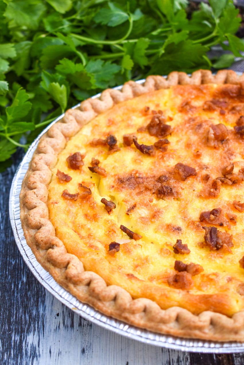 a bacon swiss quiche next to a bunch of fresh herbs