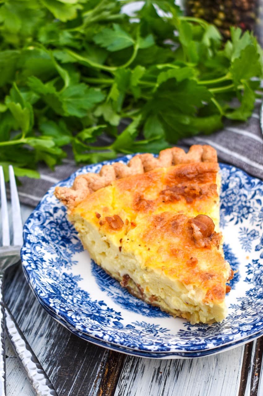 a slice of bacon swiss quiche on a blue and white tea plate