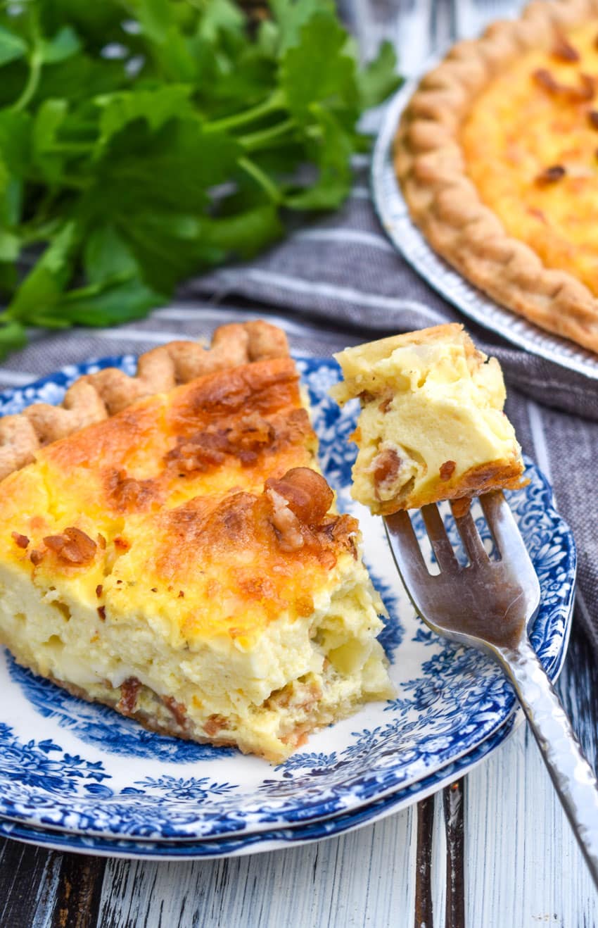a slice of bacon swiss quiche on a blue and white tea plate with a silver fork on the side