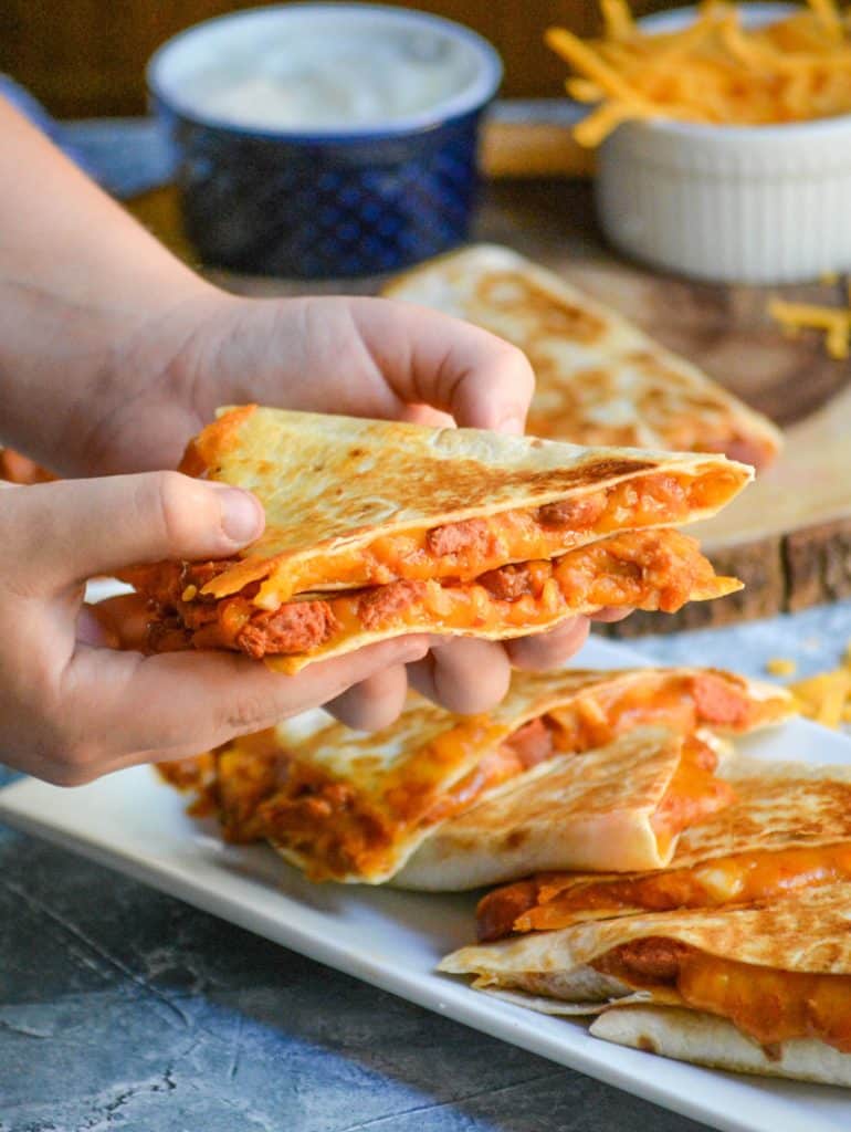 hands holding up two slices of chili cheese dog quesadillas