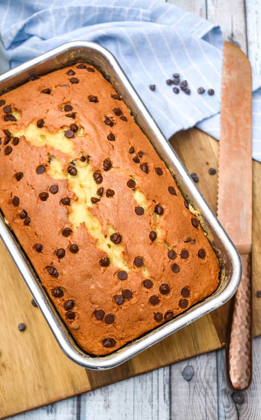 chocolate chip pound cake in a metal loaf pan sitting on a wooden cutting board