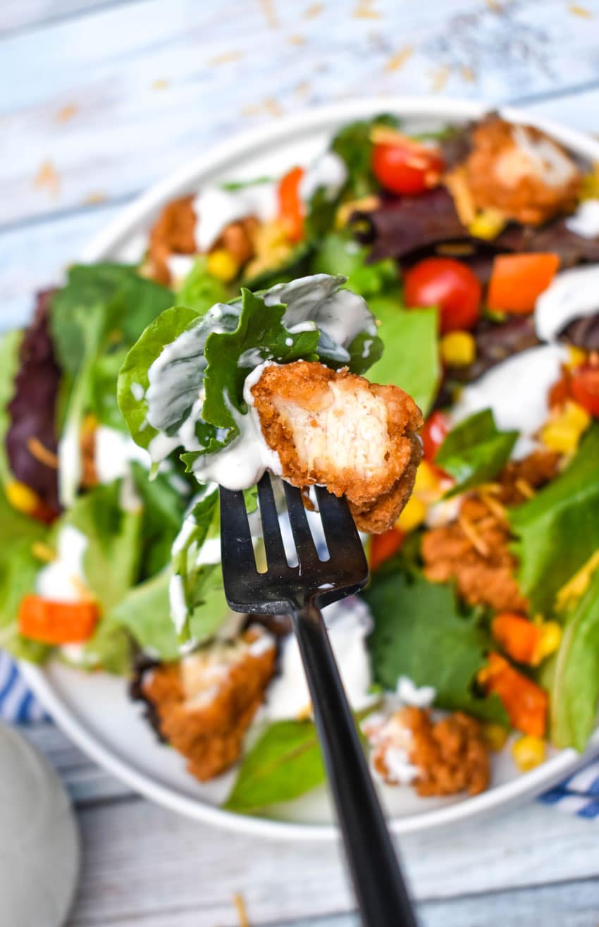 a black fork holding up cottage cheese ranch dressing coated salad leaves