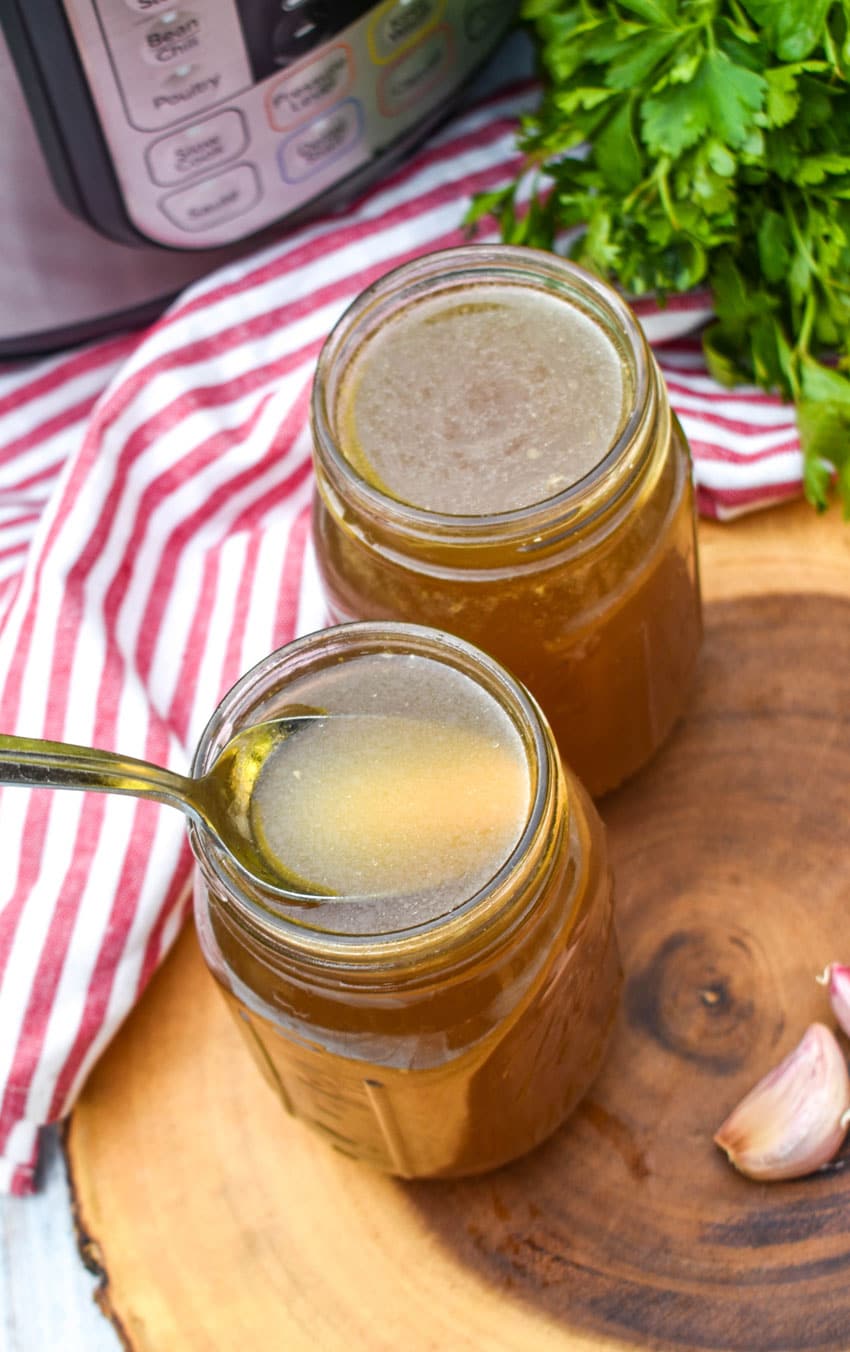 a spoon scooping instant pot chicken broth out of a glass jar