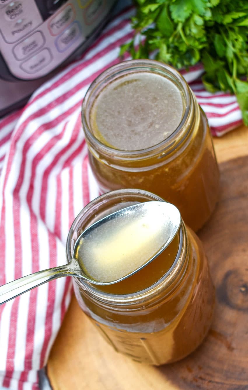 a spoon scooping instant pot chicken broth out of a glass jar