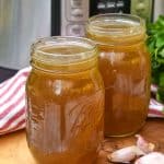 chicken broth with rotisserie chicken in two mason jars on a wooden cutting board