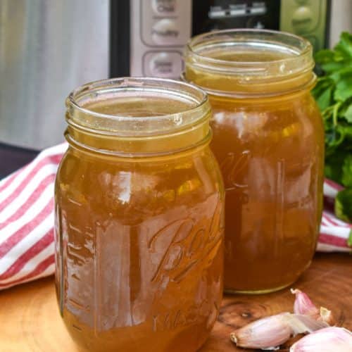chicken broth with rotisserie chicken in two mason jars on a wooden cutting board