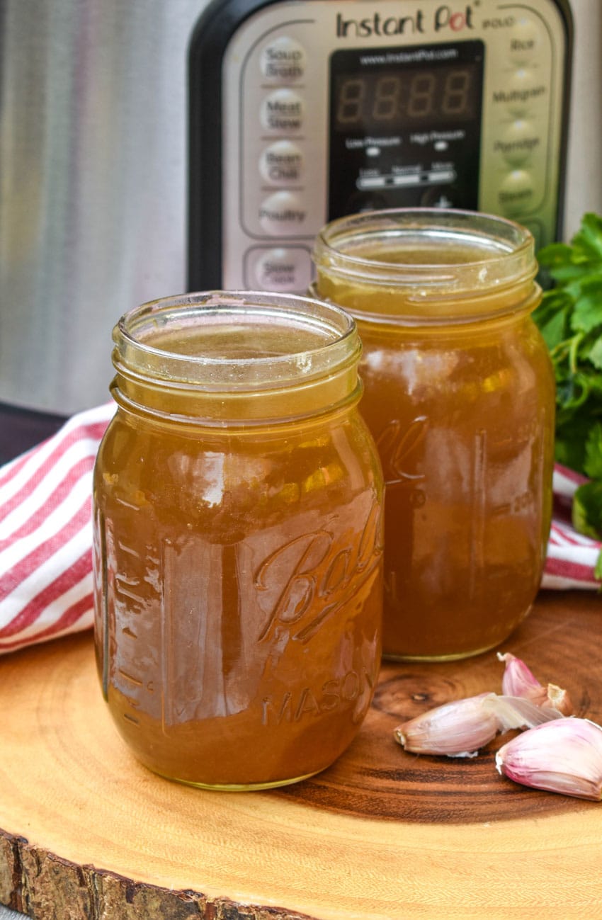 chicken broth with rotisserie chicken in two mason jars on a wooden cutting board