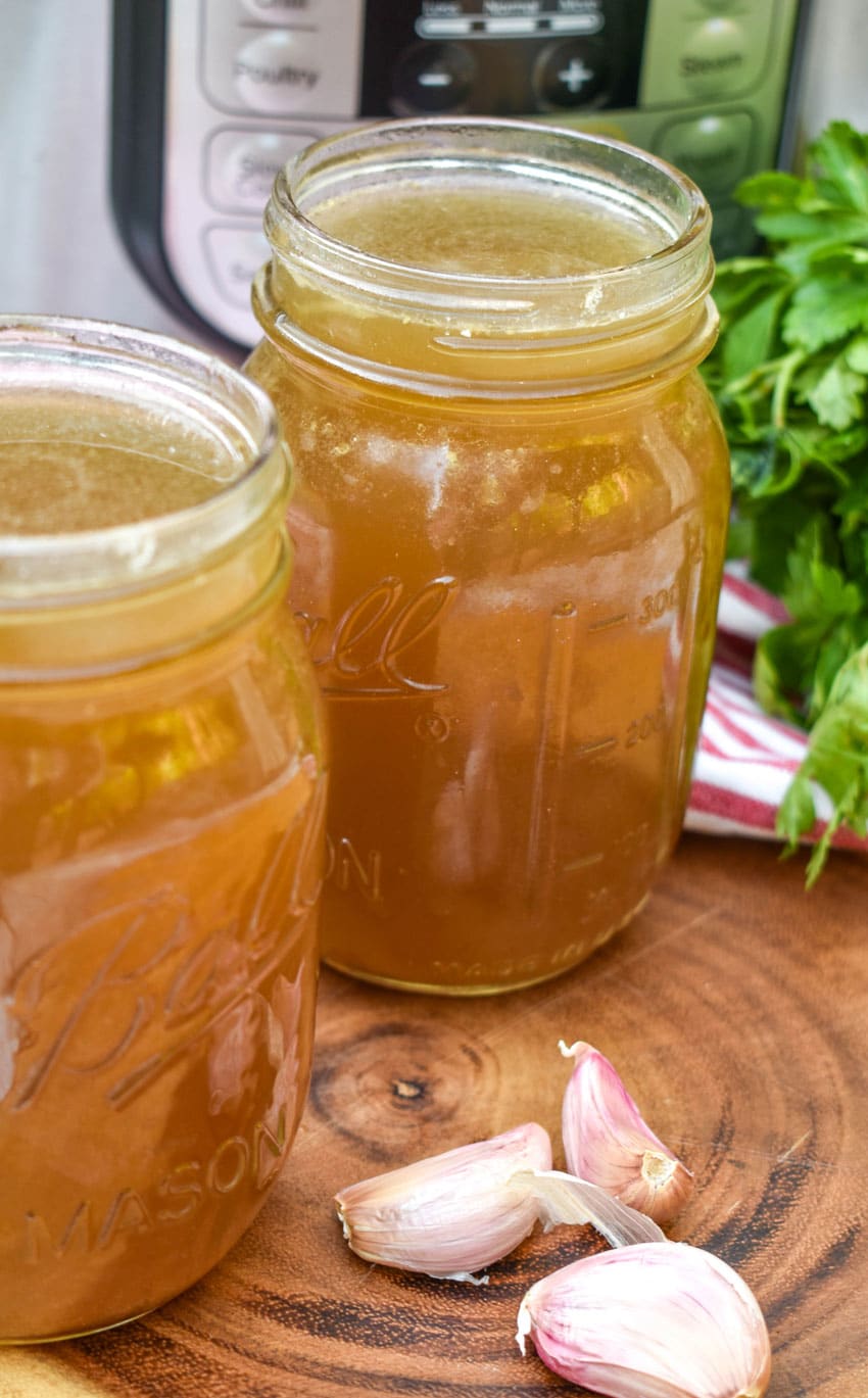 chicken broth with rotisserie chicken in two mason jars on a wooden cutting board
