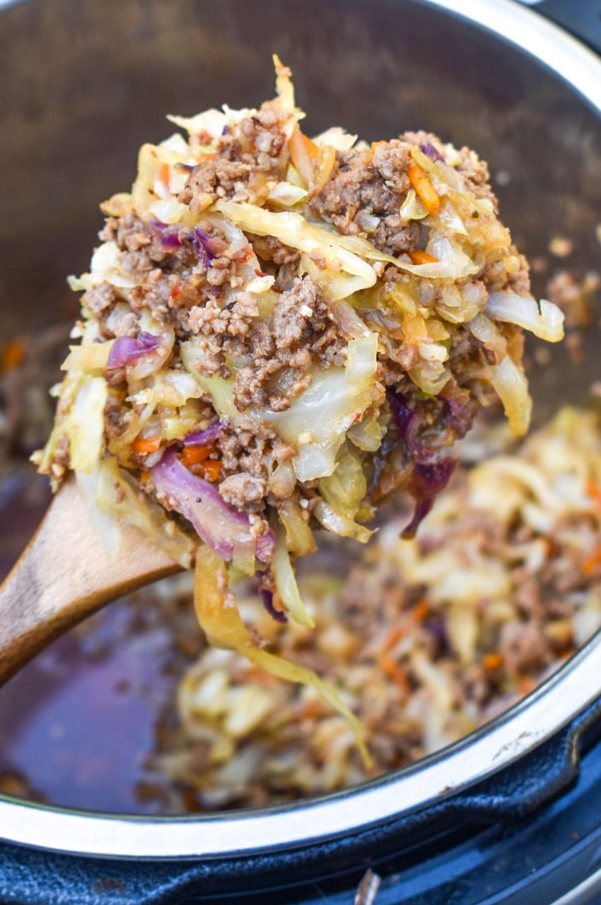 a wooden spoon scooping instant pot egg roll filling out of a pressure cooker