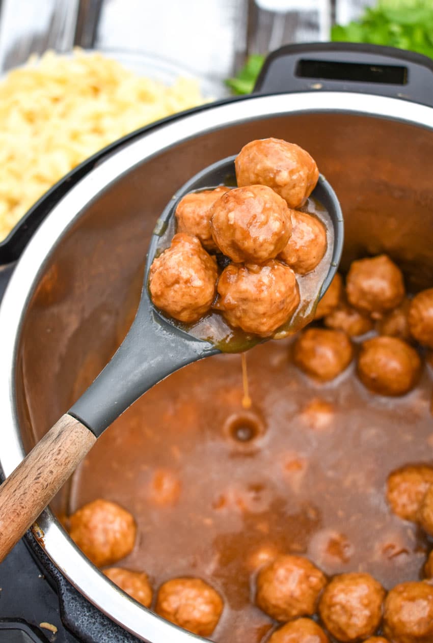 a wooden spoon holding a scoop of french onion meatballs in gravy above an instant pot