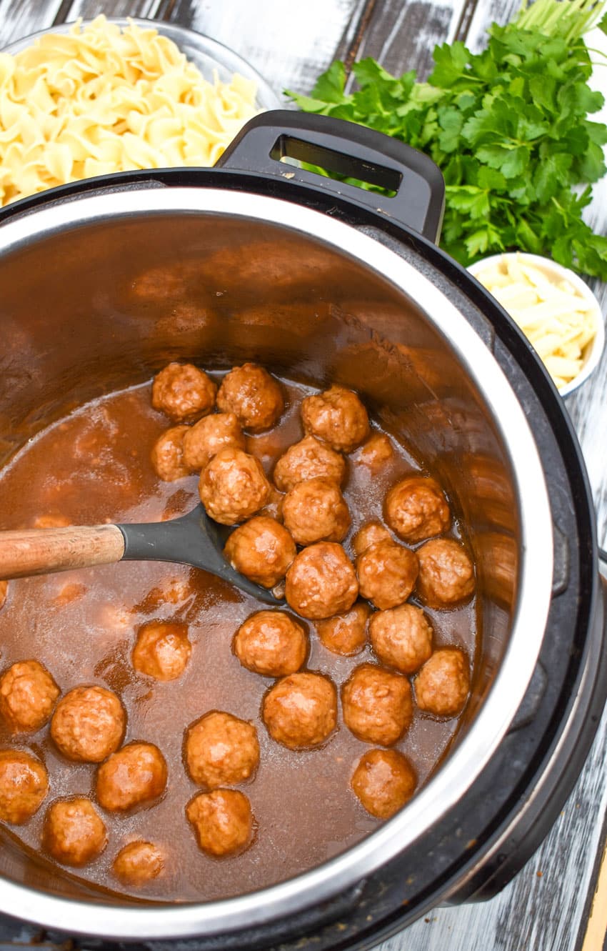 a wooden spoon in an instant pot filled with french onion meatballs in gravy