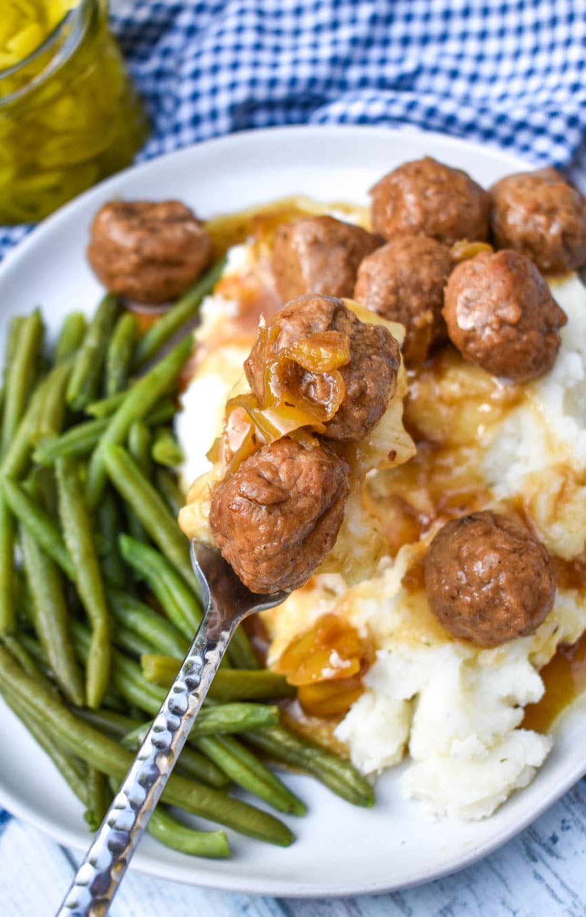 a silver fork holding up two mississippi meatballs with gravy over a white plate
