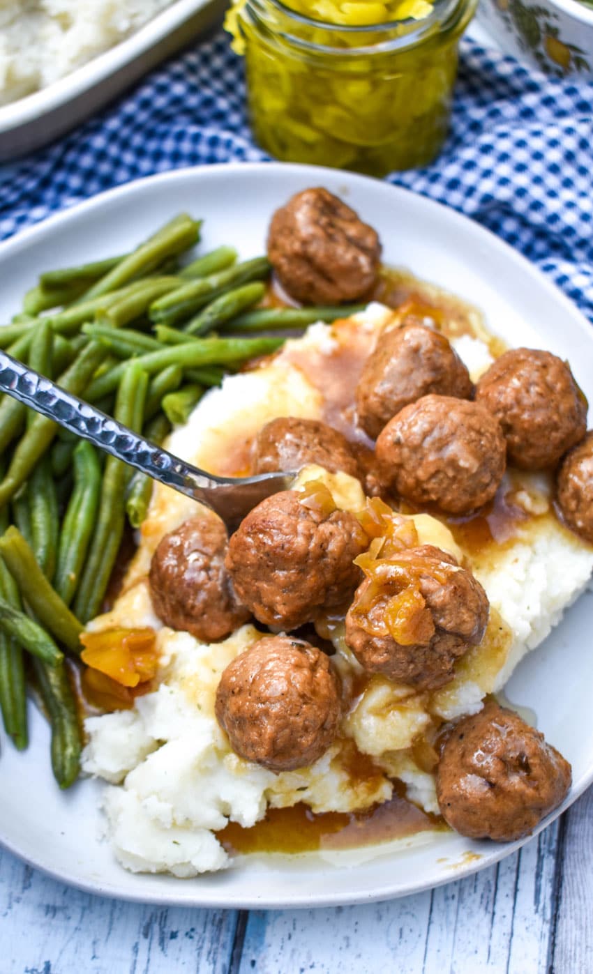 a silver fork scooping up saucy mississippi meatballs off of a white plate