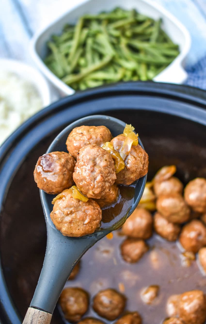 a black spoon holding up a scoop of mississippi meatballs above a black crockpot