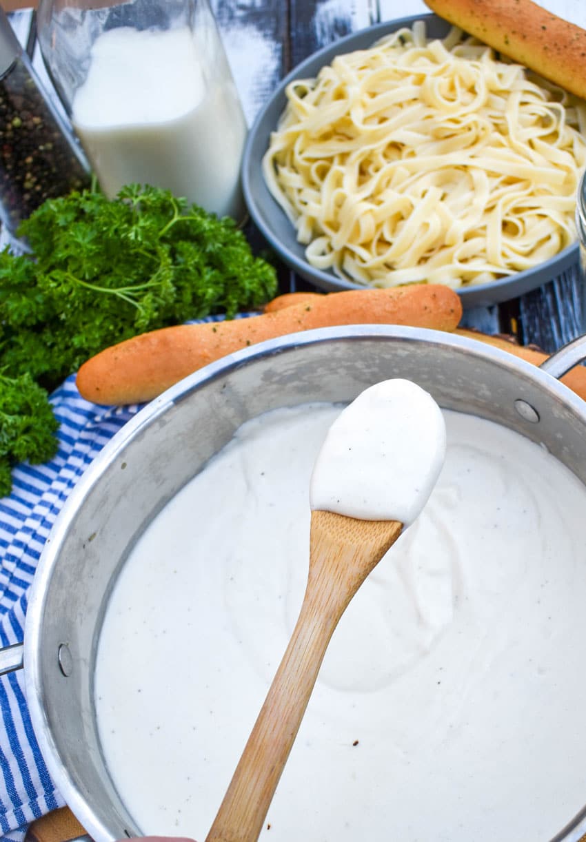 a wooden spoon scooping easy homemade alfredo sauce out of a metal sauce pan