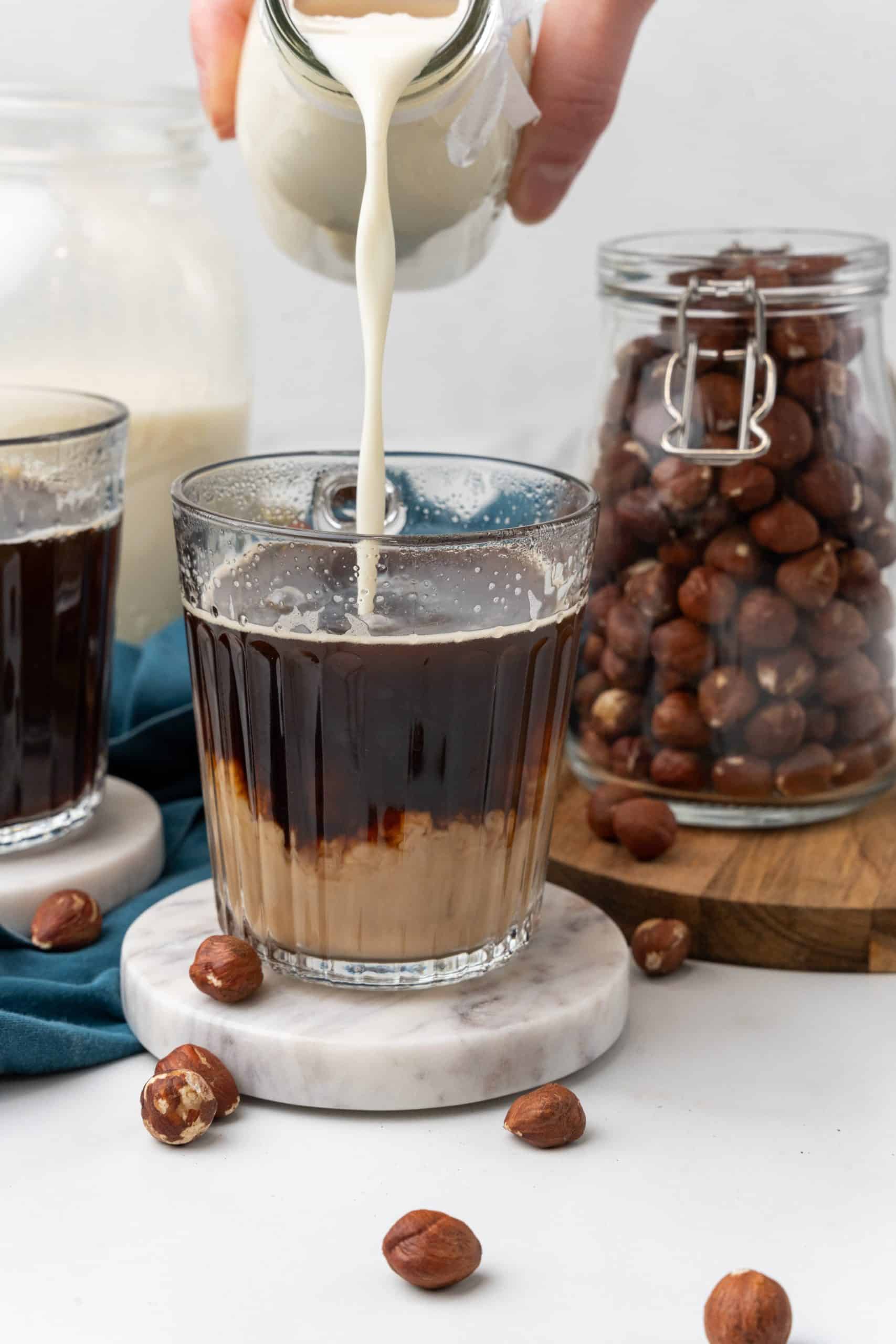 homemade hazelnut coffee creamer being poured into a glass mug filled with black coffee