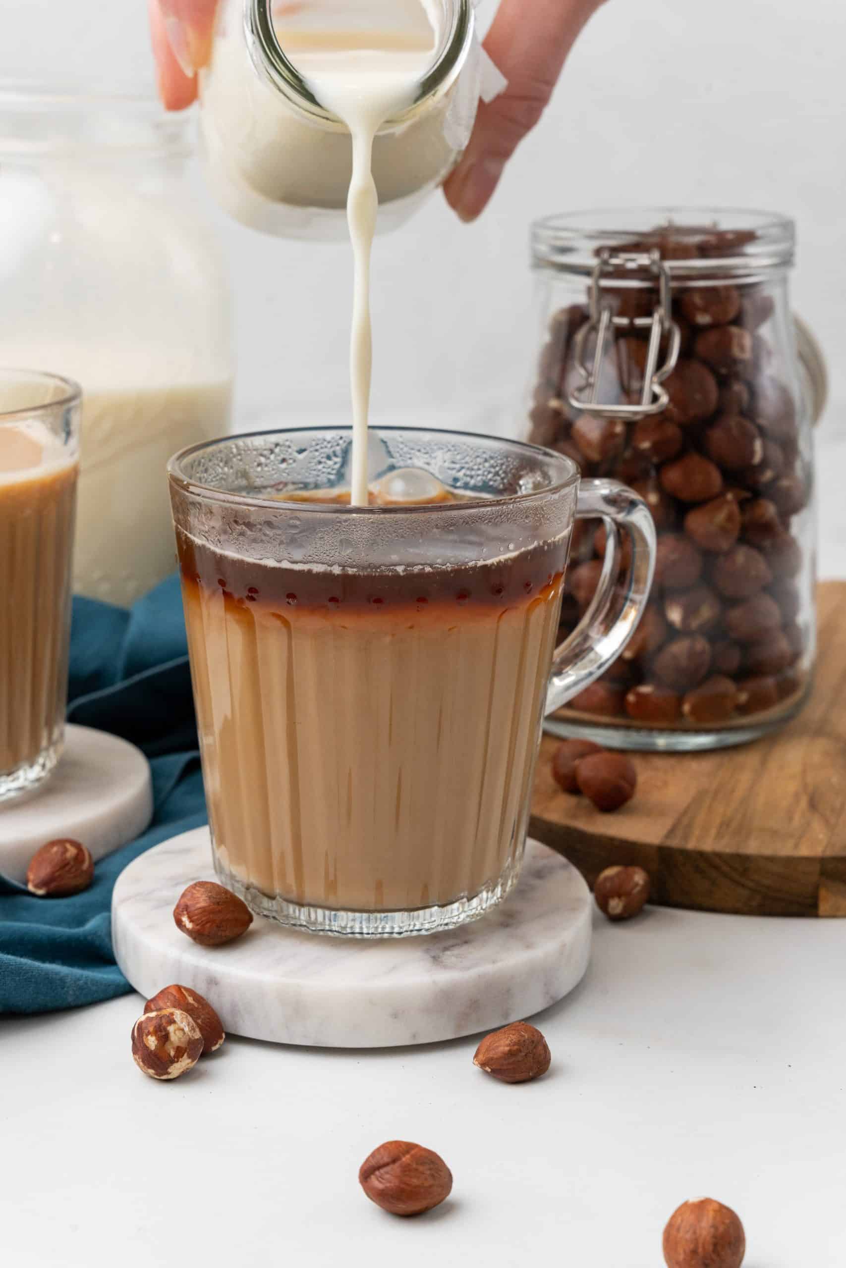 homemade hazelnut coffee creamer being poured into a glass mug filled with black coffee