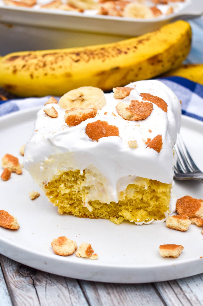 a slice of banana pudding poke cake on a white plate with a silver fork on the side