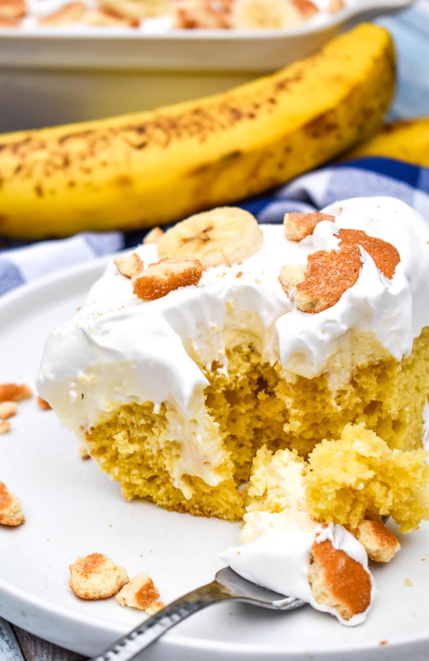a slice of banana pudding poke cake on a white plate with a silver fork on the side