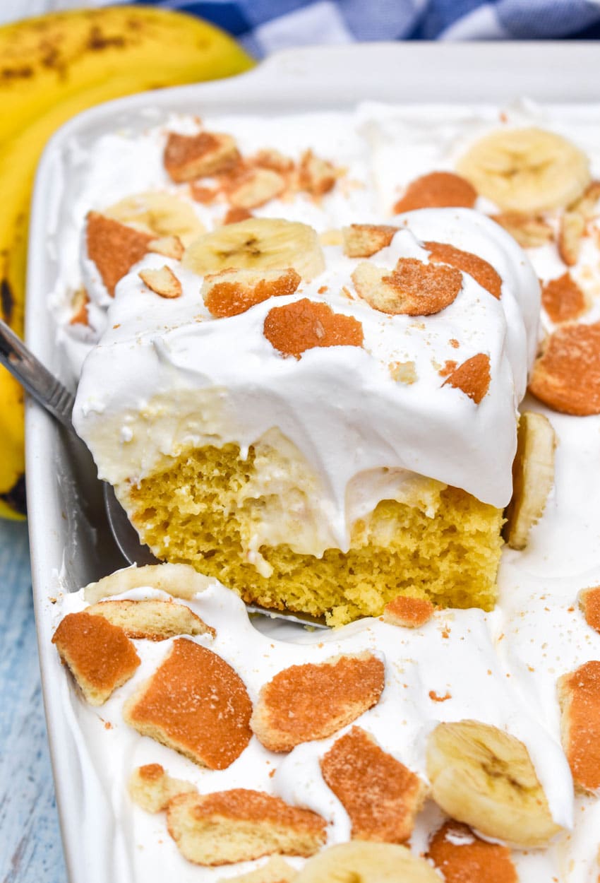 a silver spatula lifting a slice of banana pudding poke cake out of a white baking dish