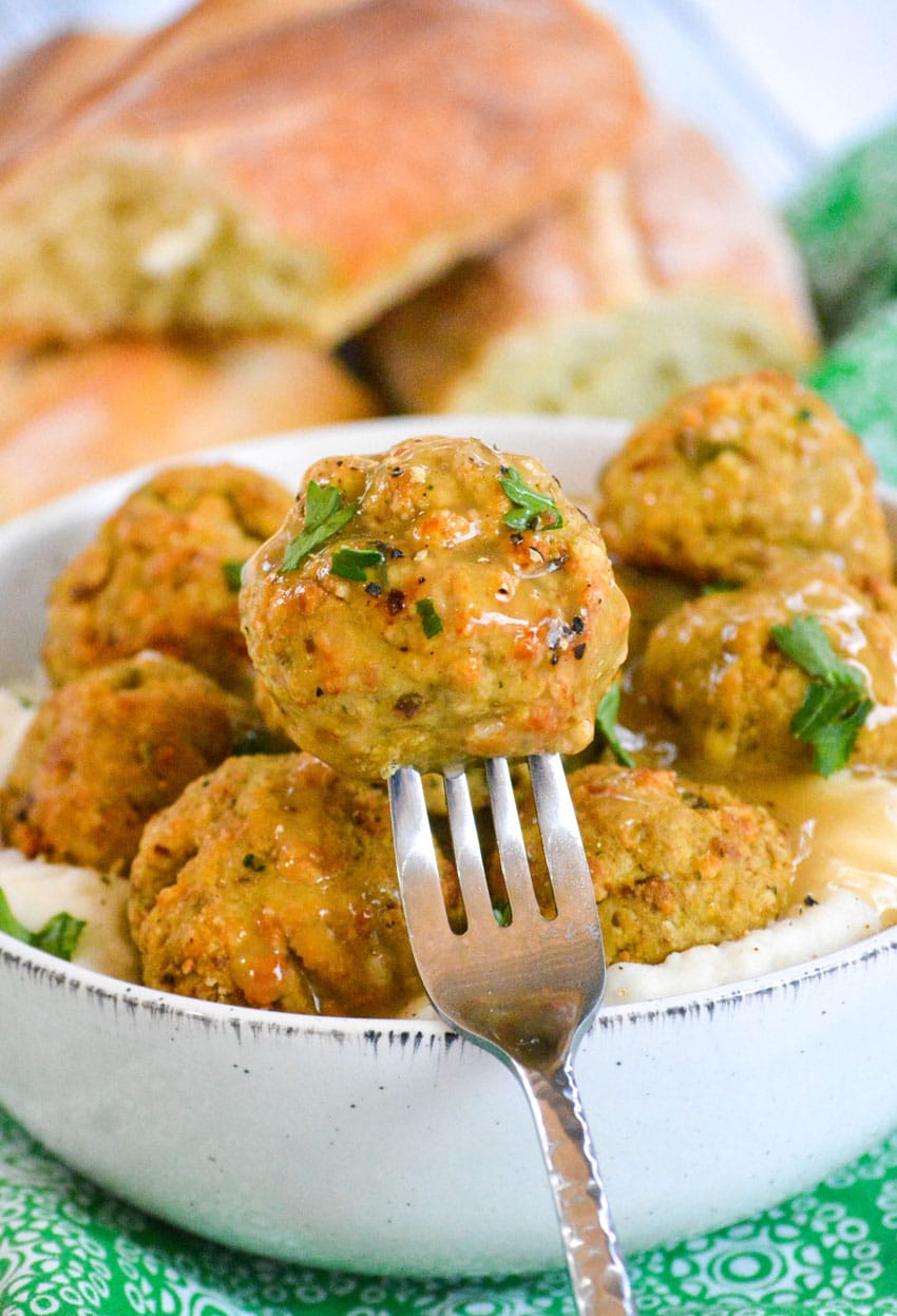 a silver fork holding up a gravy covered easy chicken meatball with stuffing mix