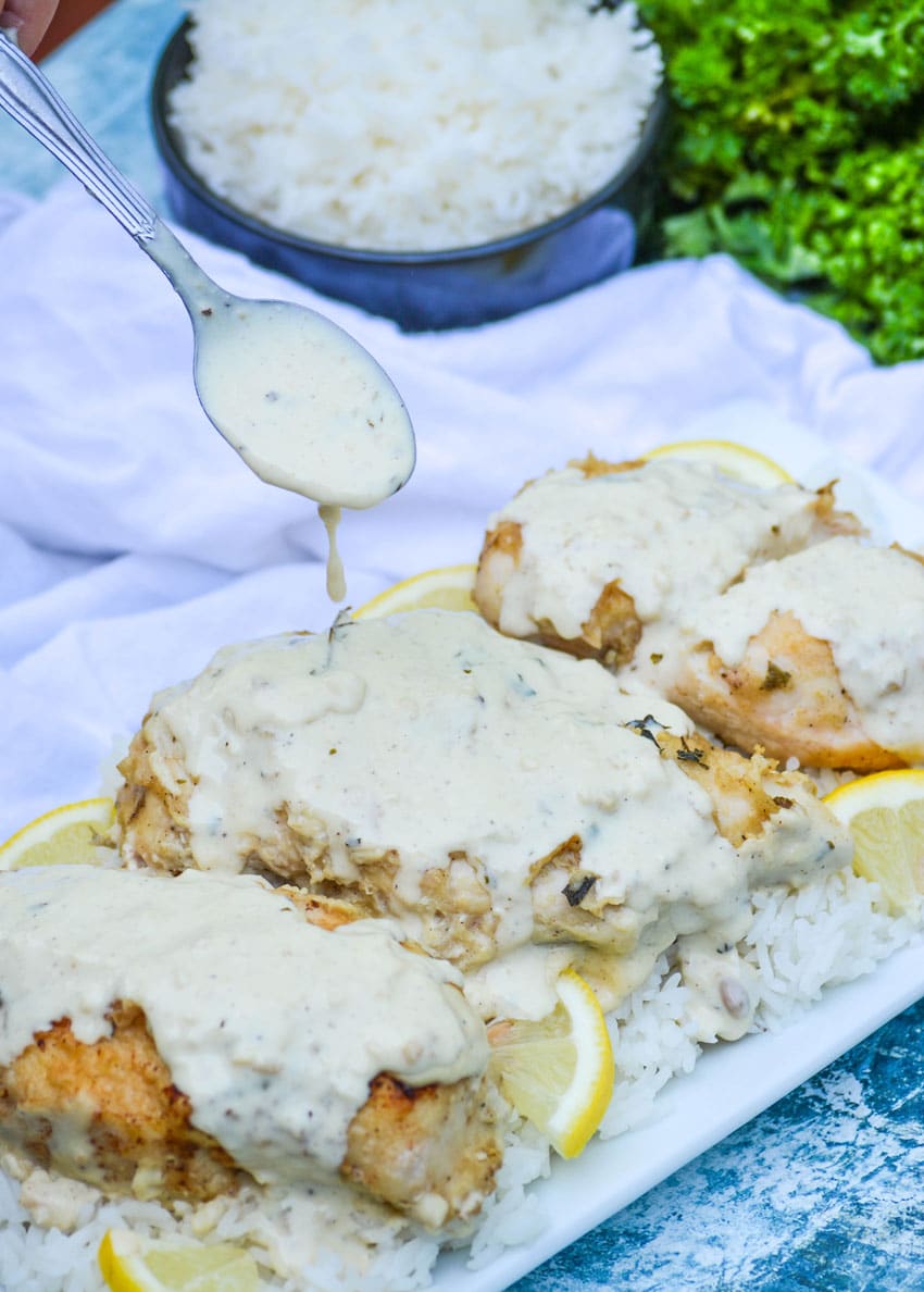 a spoon drizzling creamy lemon sauce over crispy chicken over white rice on a white platter