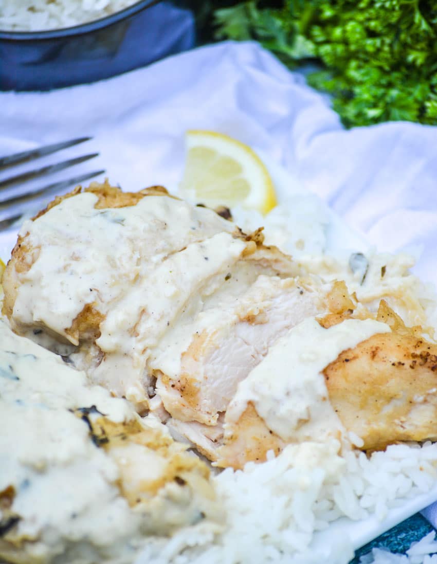 slices of creamy lemon chicken on a bed of white rice on a white plate