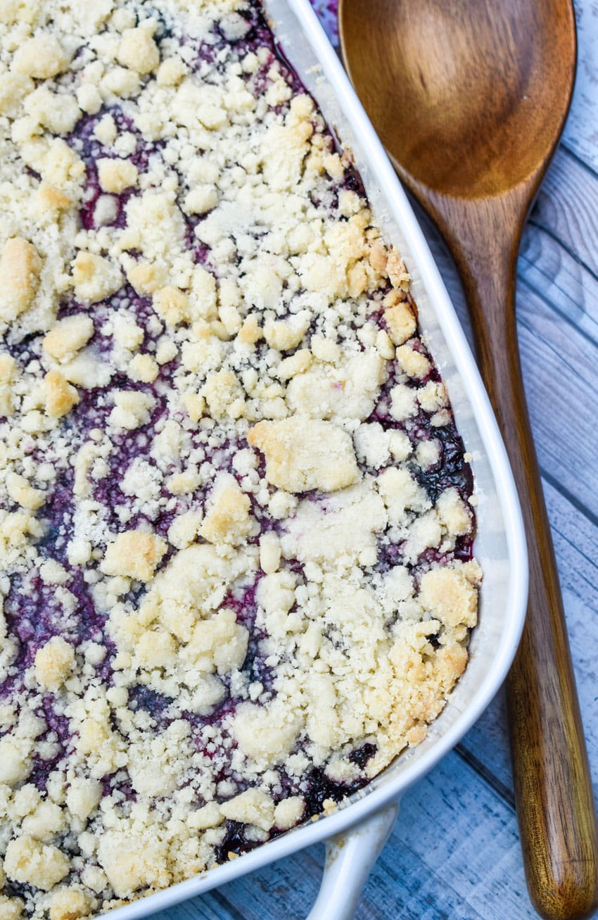 sugar cookie berry cobbler in a white baking dish with a wooden spoon on the side