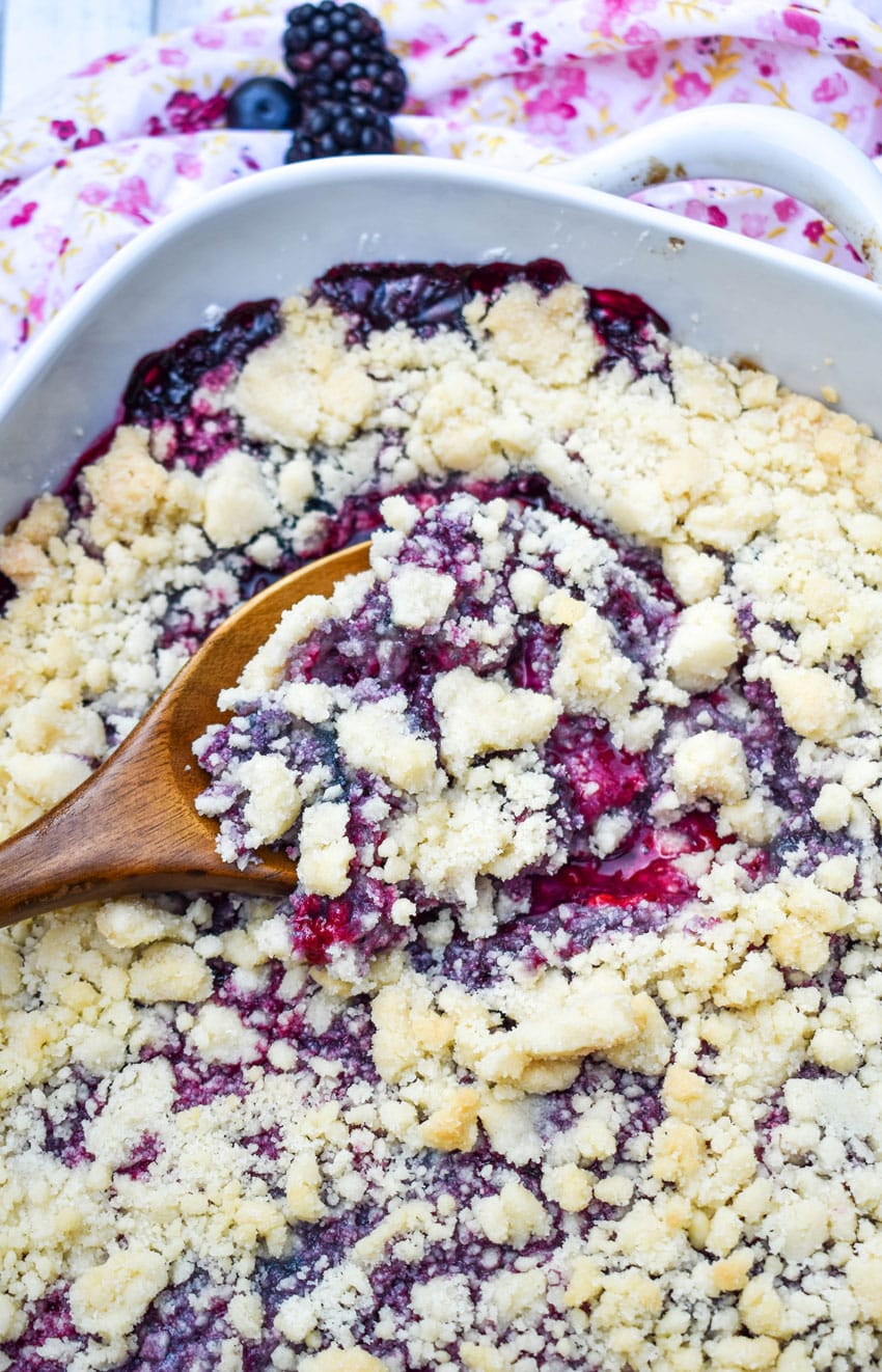 a wooden spoon scooping sugar cookie berry cobbler out of a white baking dish