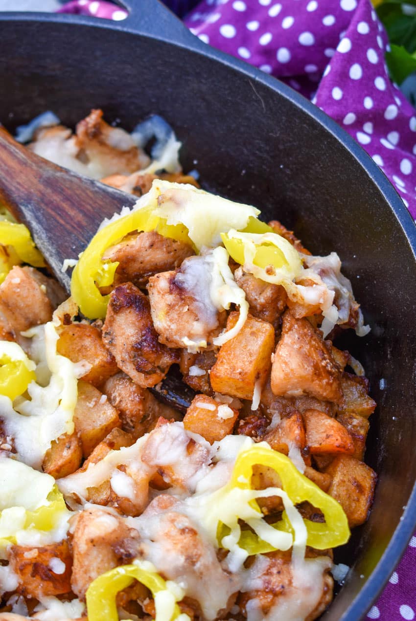 a wooden serving spoon scooping mississippi chicken and potatoes out of a black cast iron skillet