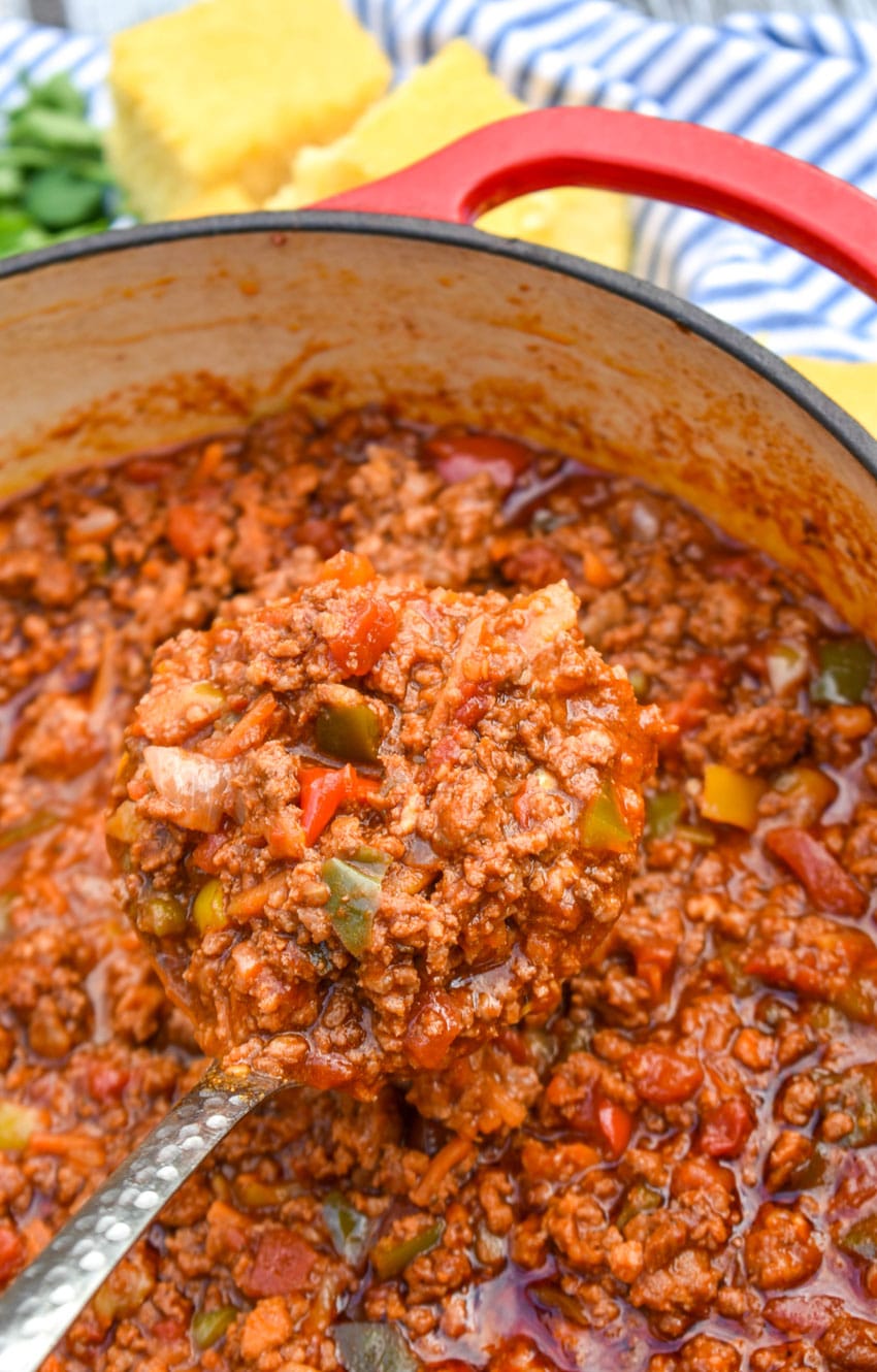 a silver ladle scooping chili without beans out of a red dutch oven