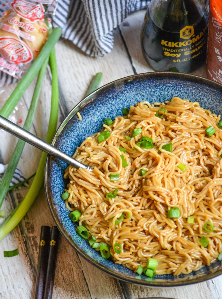 a silver fork stuck in a blue bowl filled with sesame garlic ramen noodles