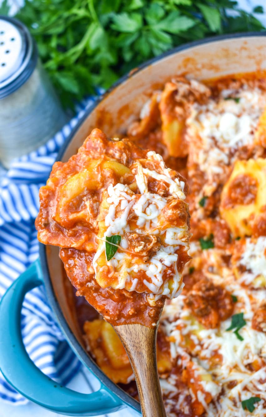 a wooden spoon scooping ravioli lasagna out of a large blue dutch oven