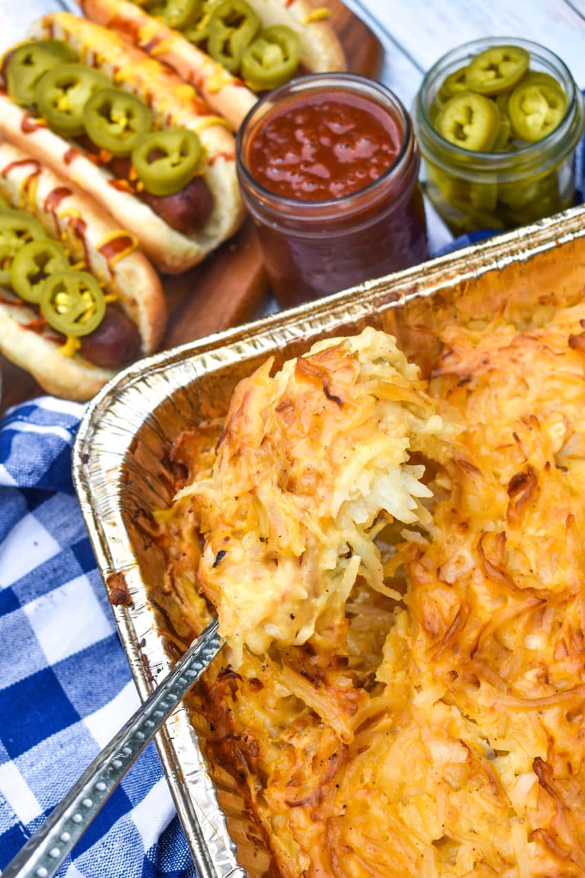 a metal spoon scooping cheesy smoked potatoes out of a disposable aluminum tin