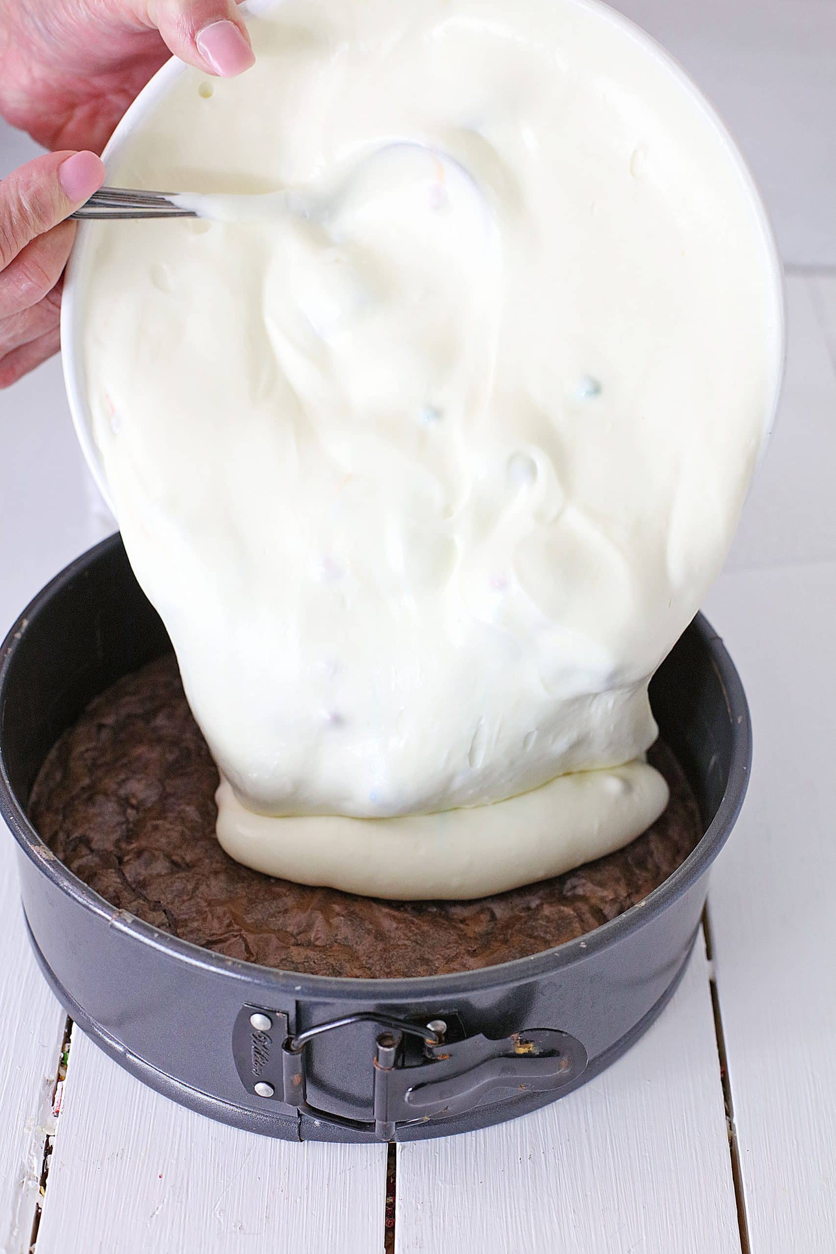 cheesecake filling being poured over a brownie crust into a springform pan