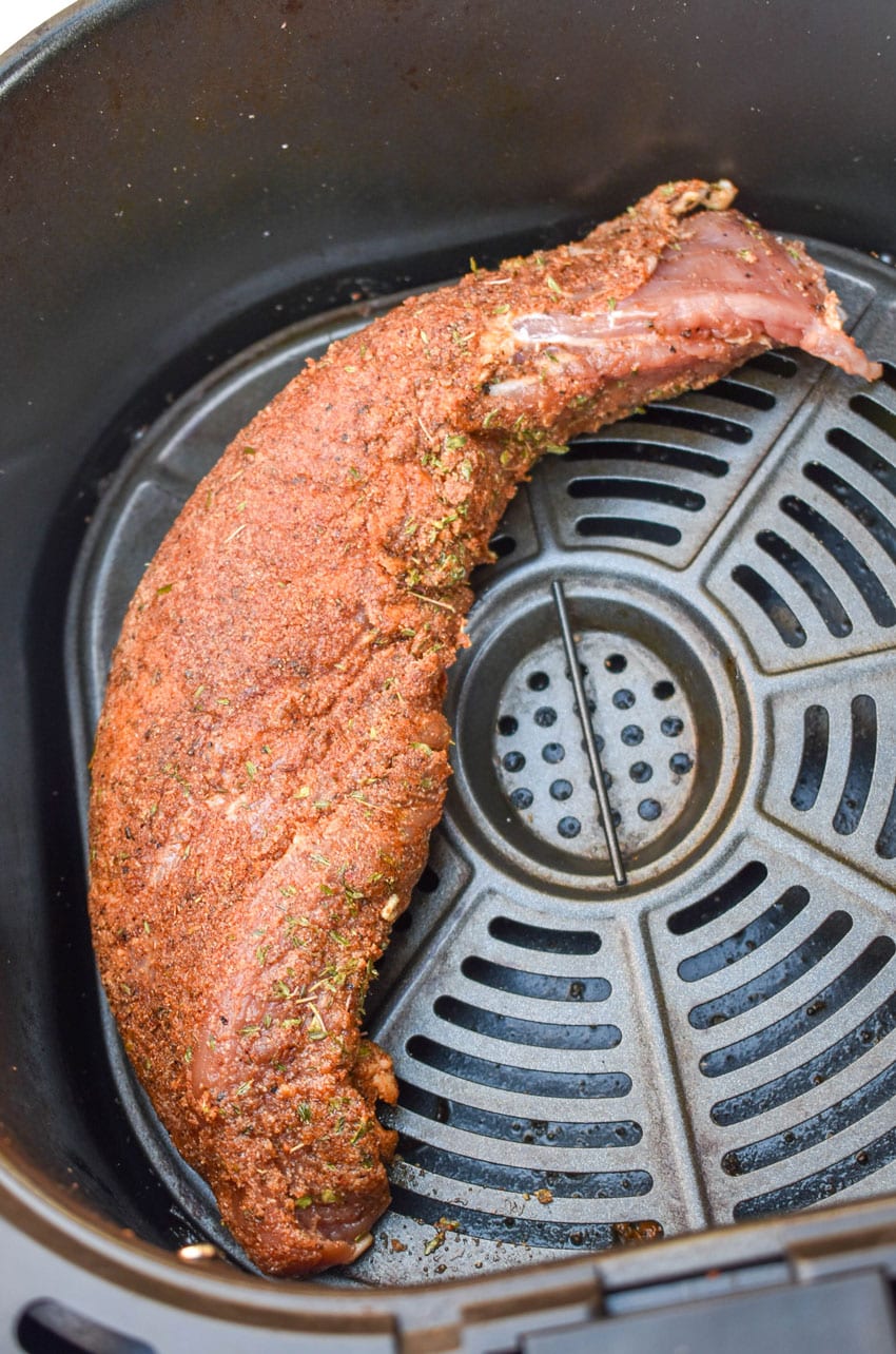 seasoning rubbed raw pork tenderloin in the basket of an air fryer