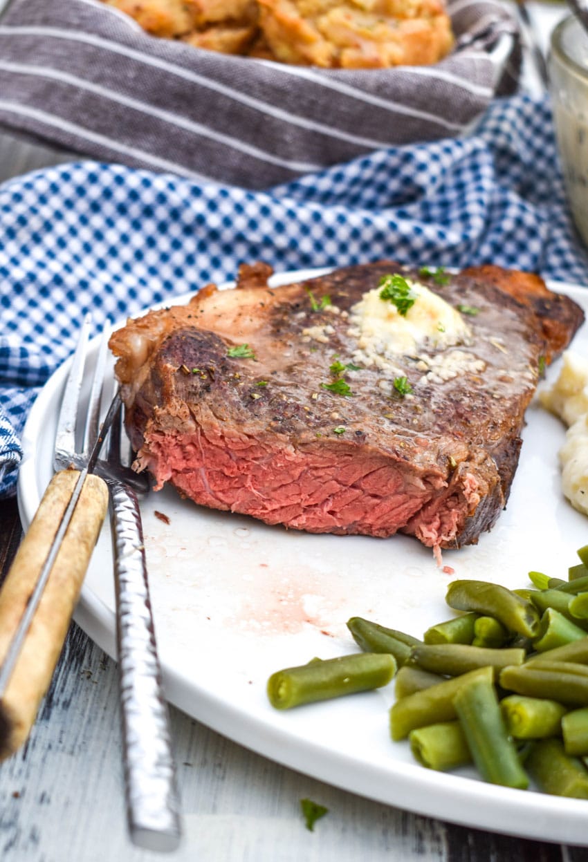 a cut air fried steak on a white dinner plate with a silver fork on the side